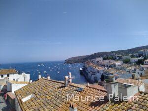Vue aérienne de Cadaqués avec les maisons blanches, les toits en tuiles et les barques dans la baie.