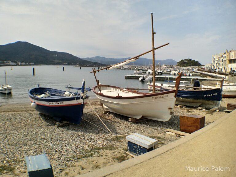 Pointus tirés au sec près du port, avec mer et montagne en arrière‑plan.
