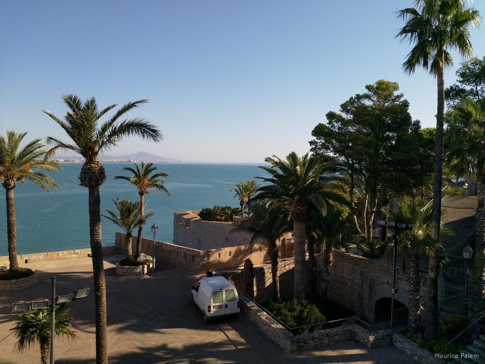Vue de Peñíscola depuis le château del Papa Luna, avec les palmiers, les remparts et la Méditerranée en arrière‑plan.