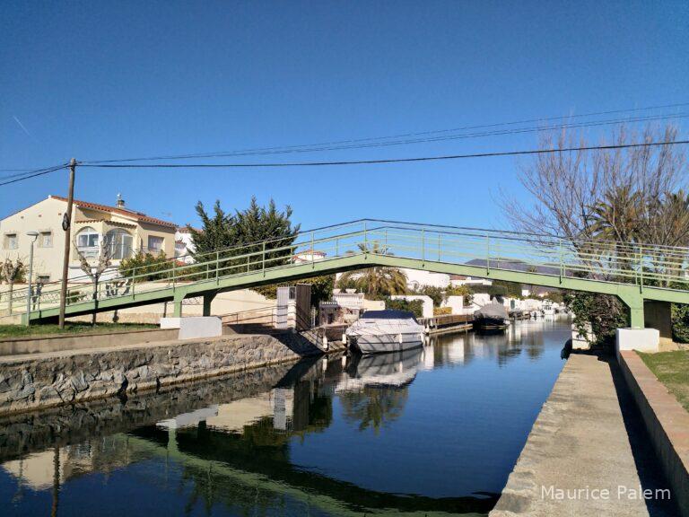 Vue d'un canal d'Empuriabrava avec une passerelle piétonne et des résidences en bord d'eau illustrant la coexistence entre habitants permanents, résidences secondaires et activité touristique.